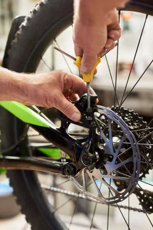 Cropped shot of male mechanic working in bicycle repair shop, installing brakes using special tool