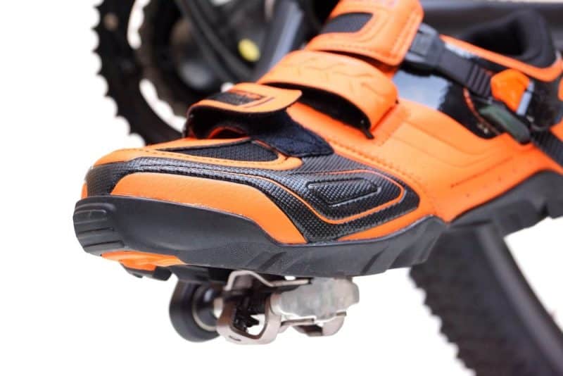 Mountain bike cycling shoes in orange color on clipless pedal isolated