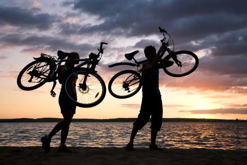 man and woman silhouette carrying bikes